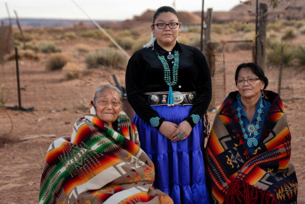 Three generation women, with two grandmothers and a granddaughter, all native American Navajo women sitting and posing in a group outside