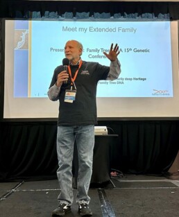 Bennett Greenspan, founder of FamilyTreeDNA, stands on stage delivering a presentation at the 15th International Conference on Genetic Genealogy (ICGG) in 2023. The screen behind him reads “Meet my Extended Family.”