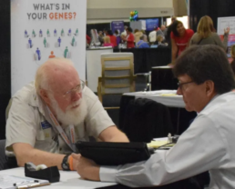 Bob McLaren, a beloved leader in the genetic genealogy community, sits at the FamilyTreeDNA booth during the 2011 FGS Conference, engaging with a fellow attendee. McLaren was known for his wisdom, kindness, and unmatched dedication to surname projects.