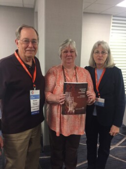 Jim Bartlett stands with fellow genealogists at the 15th International Conference on Genetic Genealogy, holding the book Advanced Genetic Genealogy.